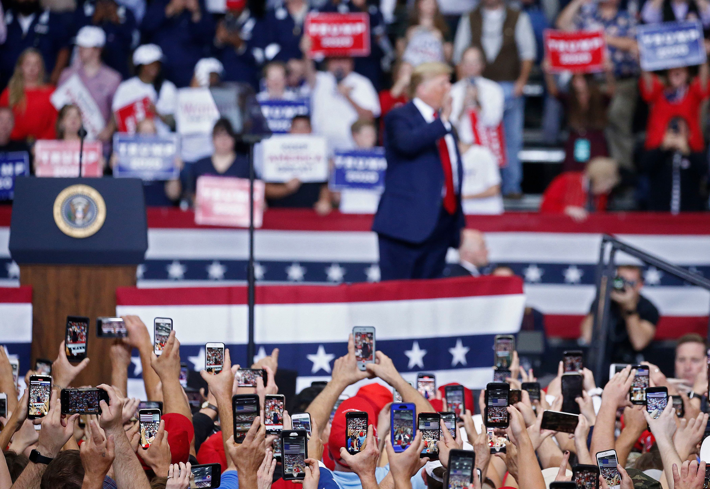 People use their phones to photograph President Donald Trump as he addresses a rally in Monroe, La., on Nov. 6