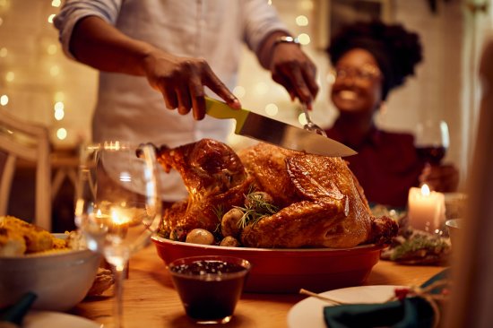 Close-up of African American man carving roasted Thanksgiving turkey.