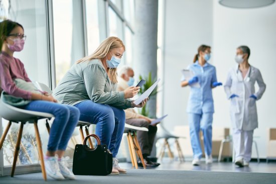 Woman with face mask using smart phone while reading her medical report in waiting room at the clinic.