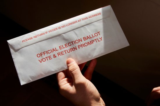 A person standing inside his home holding his mail in voting ballot