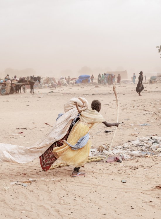 A girl runs carrying her belongings in search of a shelter to hide from the sandstorm and the looming rain in Adré refugee camp.