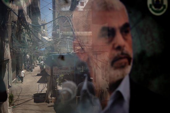 People are reflected in a window displaying a poster of Hamas leader Yahya Sinwar in the Palestinian camp of Bourj al-Barajneh on Aug. 8, 2024.